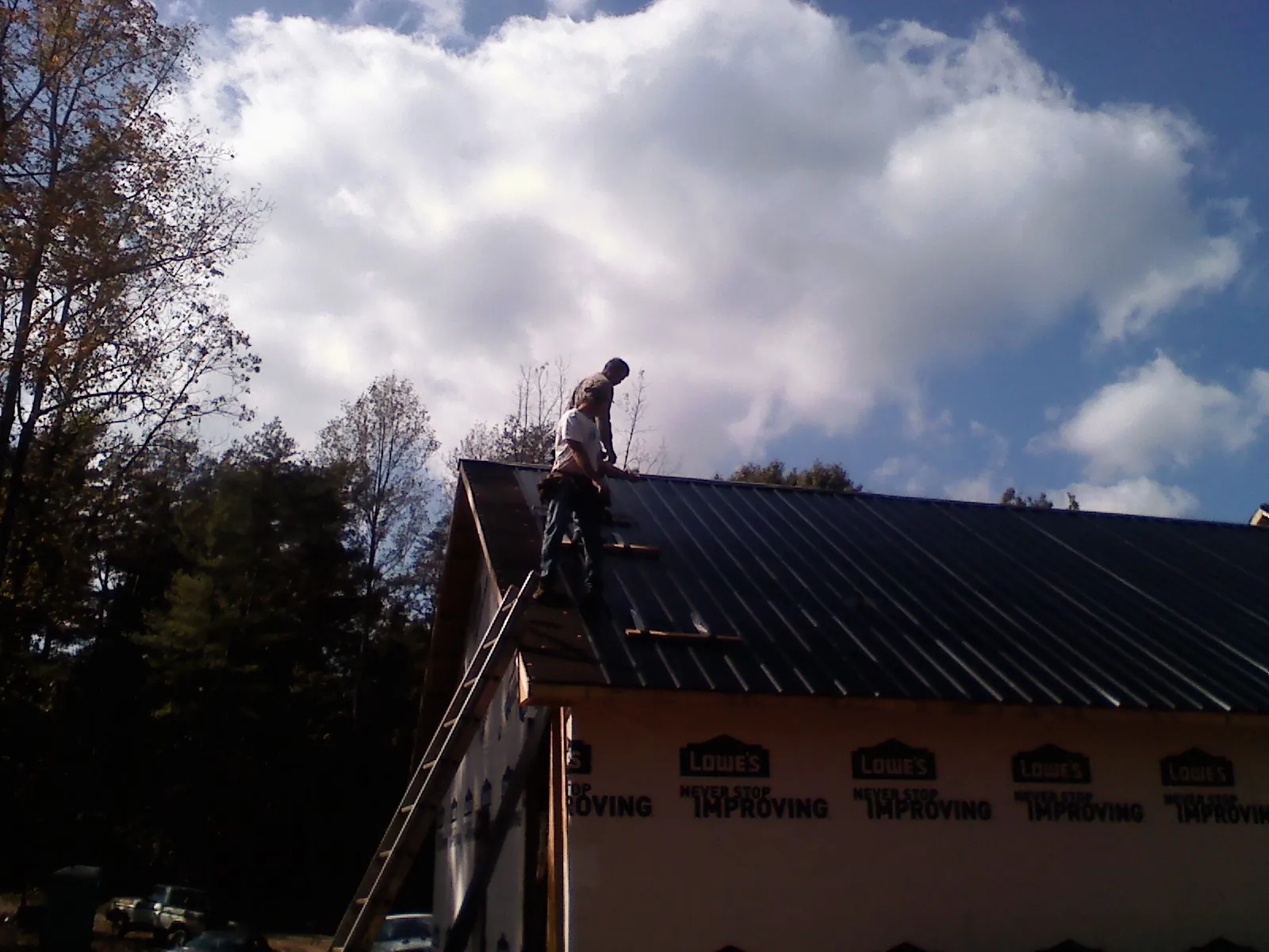 Roofer fastening dark metal panels high against a cloudy sky, from a Roof Inspection job in Dumont